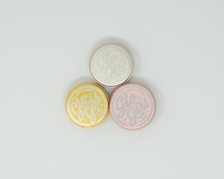The Glo Girl family — three rose-gold tins of organic lip and body balm arranged on a soft surface.